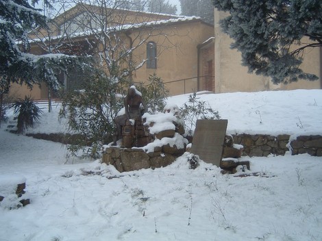 Monumento della Panca in un paesaggio innevato, circondato da alberi e una struttura rustica sullo sfondo.