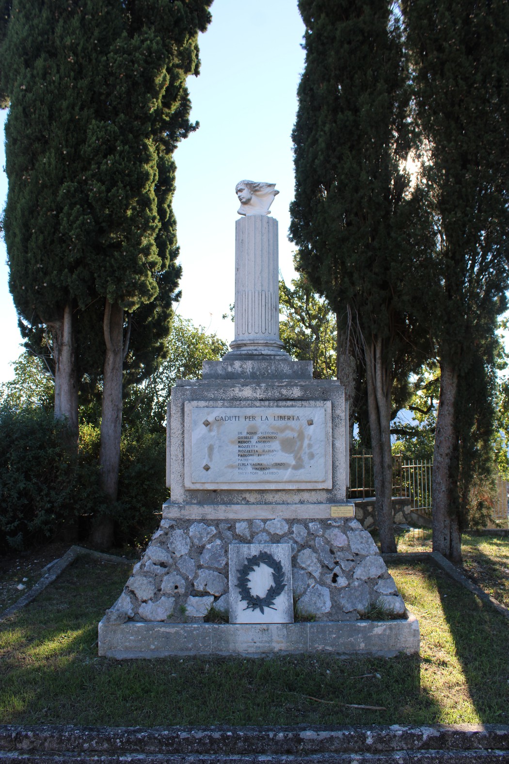 Monumento ai caduti per la libertà, decorato con una scultura su colonna e circondato da vegetazione.