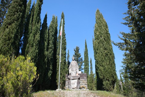 Monumento ai caduti di Purocielo circondato da alberi di cipresso e con una bandiera tricolore in evidenza.