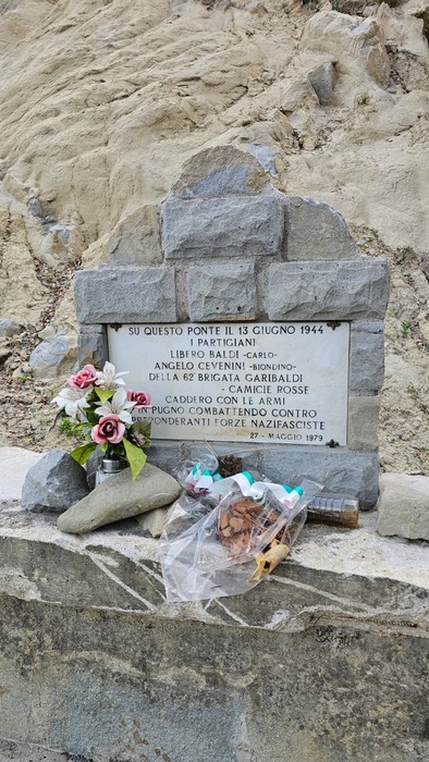 Monumento in memoria di Baldi e Cevenini, con fiori, situato in un'area naturale.