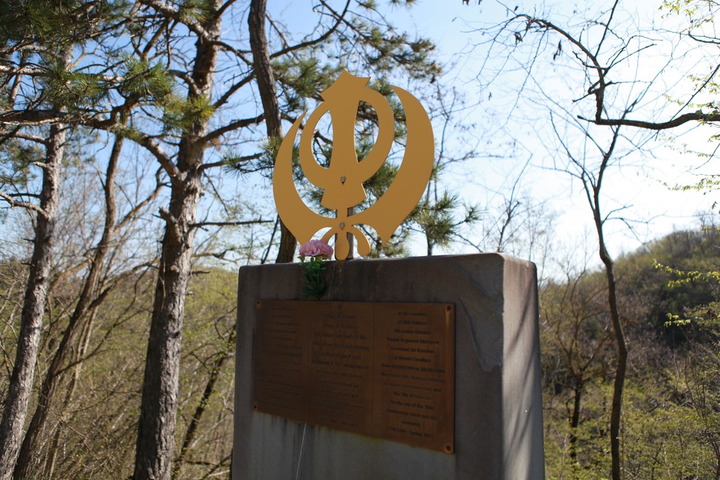 Monumento commemorativo con simbolo dorato, circondato da alberi e natura, dedicato alla Battaglia della Cavallara.