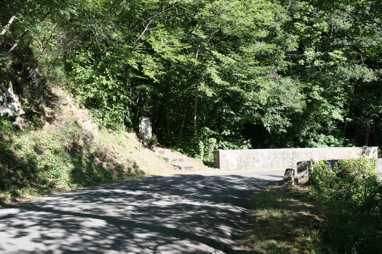 Cippo di Mòdine: monumento immerso nella natura, lungo una strada circondata da alberi e ombre.