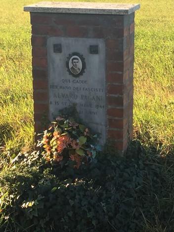 Cippo commemorativo dedicato ad Alvaro Pagani, martire antifascista, con fiori e vegetazione circostante.