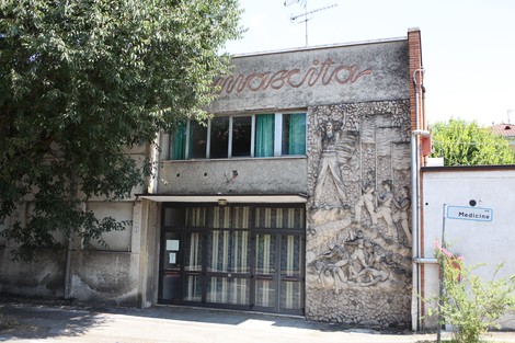 Bassorilievo decorativo sul muro di un edificio, rappresentante figure stilizzate in un contesto artistico.
