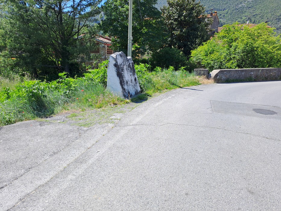 Cippo a Pacchini situato lungo una strada, circondato da vegetazione e elementi naturali.