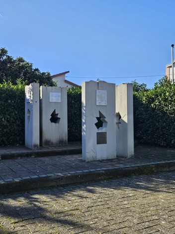 Monumento alla Resistenza con elementi architettonici incisivi, circondato da verde e illuminato da un cielo azzurro.