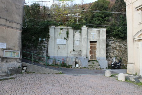 Lapide a Ricchini, struttura semplice in un ambiente urbano con vegetazione e sterrato circostante.