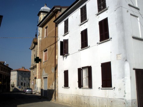 Lapide commemorativa di Fugazza Mario in una via storica, con edifici caratteristici e cielo sereno.