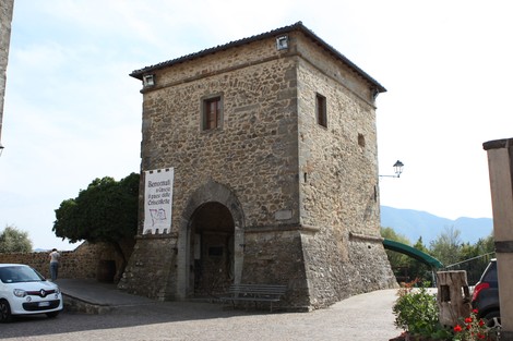 Lapide ai caduti di Cascio, monumento in pietra con torre storica, circondato da un'area verde e fiorita.