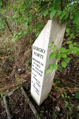 Cippo memoriale dedicato a Sergio Forti, medaglia d'oro al valore militare, immerso nella natura.