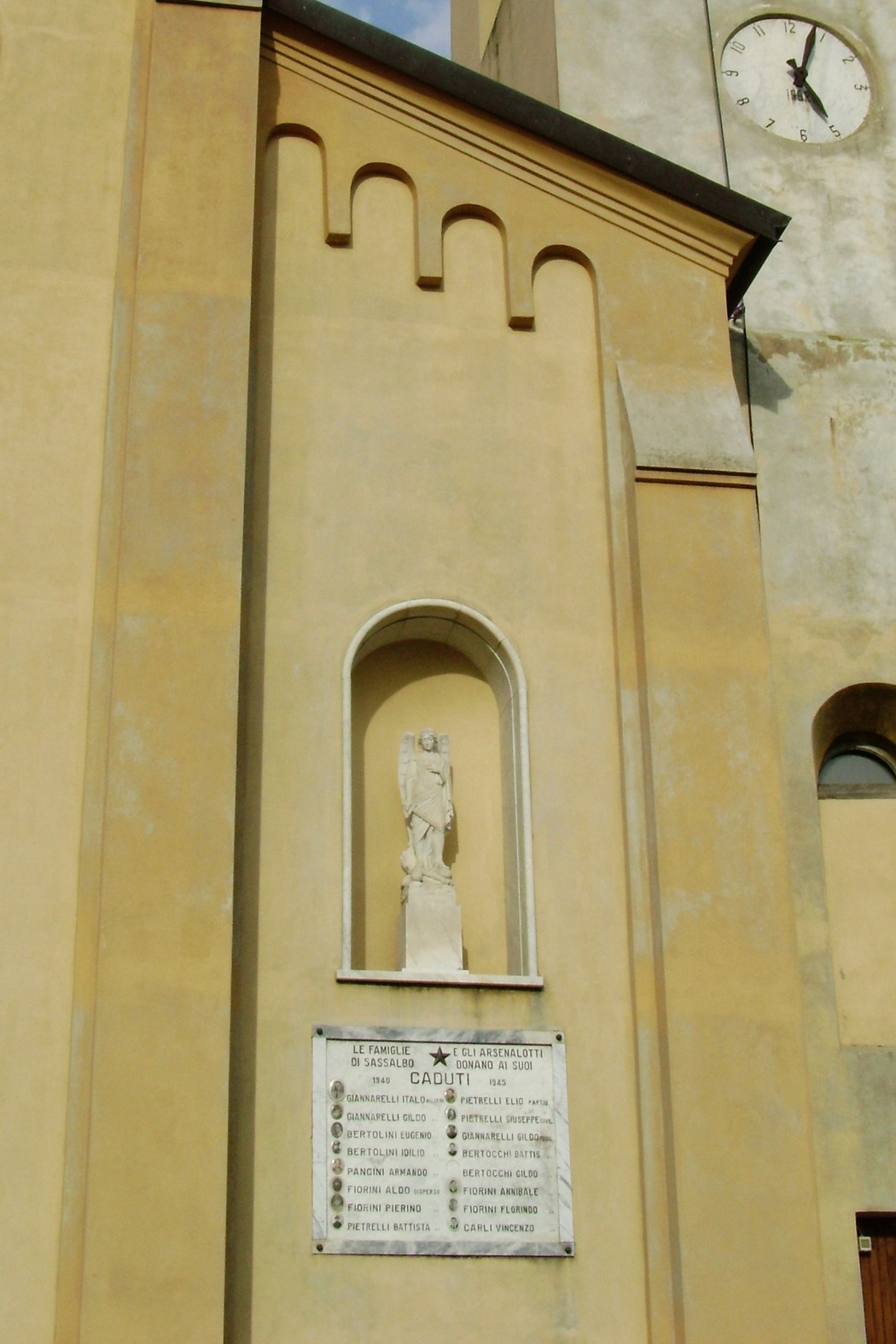 Lapide commemorativa ai caduti di Sassalbo, affiancata da una statua e situata su un edificio storico.