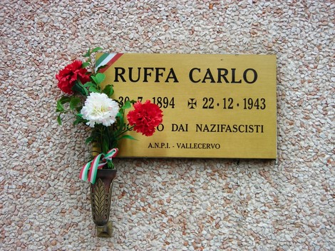 Targa commemorativa a Carlo Ruffa, vittima dei nazifascisti, decorata con fiori e simboli della resistenza.