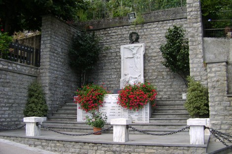 Monumento ai caduti di Levigliani, con lapide commemorativa e fiori, circondato da una cornice di pietra.