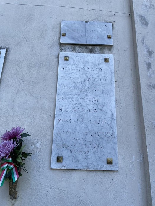 Lapidi commemorative dei caduti di Savonera, con fiori e decorazioni tricolori.