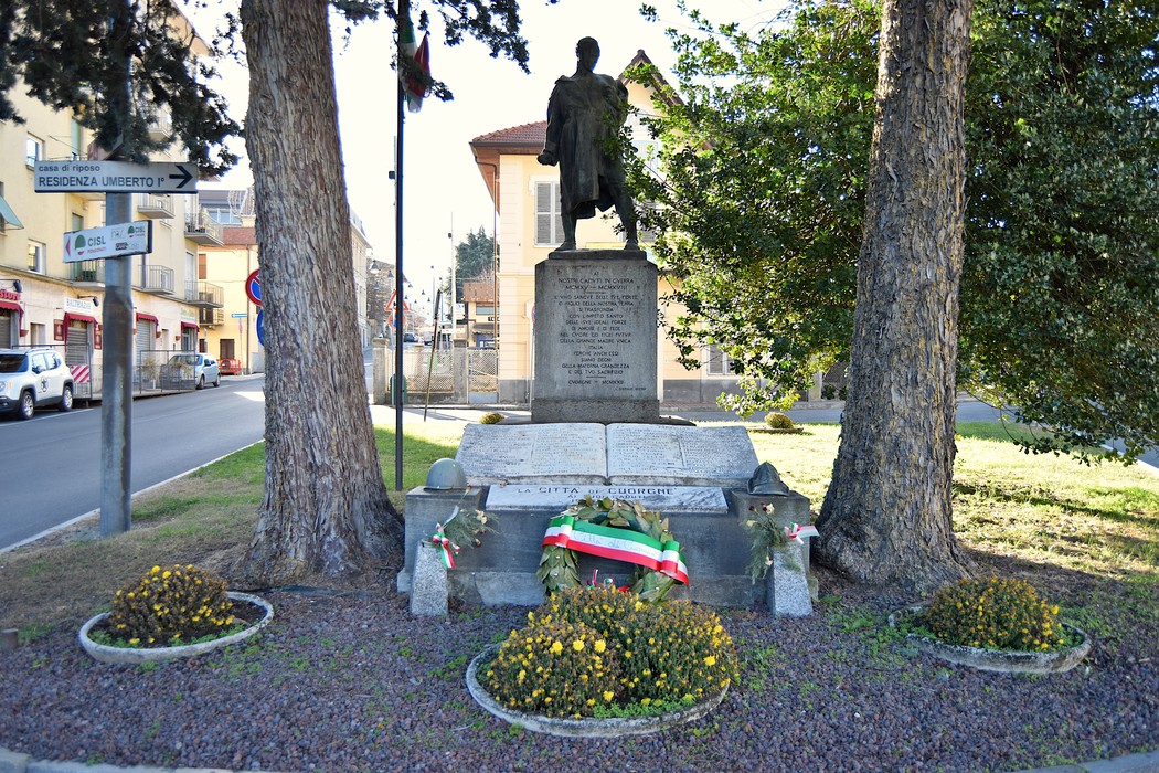 Monumento ai caduti, con statue e corona d'alloro, circondato da alberi e fiori. Rappresenta la memoria storica locale.