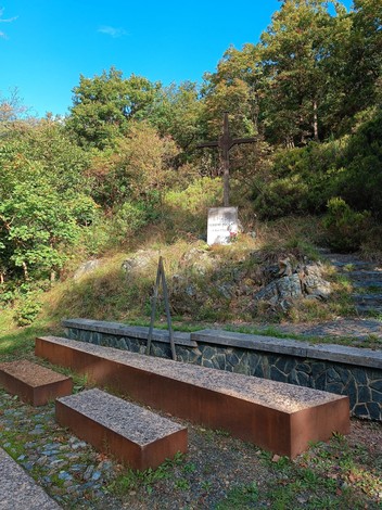 Croce ai caduti della Benedicta, memoriale immerso nella natura, con panchine circondate da alberi e arbusti.
