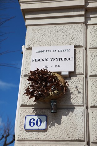 Lapide commemorativa di Remigio Venturoli, situata su un muro, con una corona di foglie decorative.