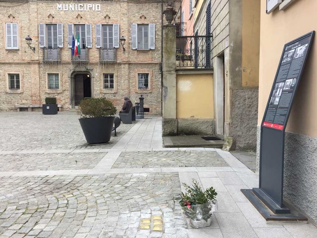 Pietre d'inciampo in memoria di Bozzi, Capitani e altri, visibili in una piazza con il municipio sullo sfondo.