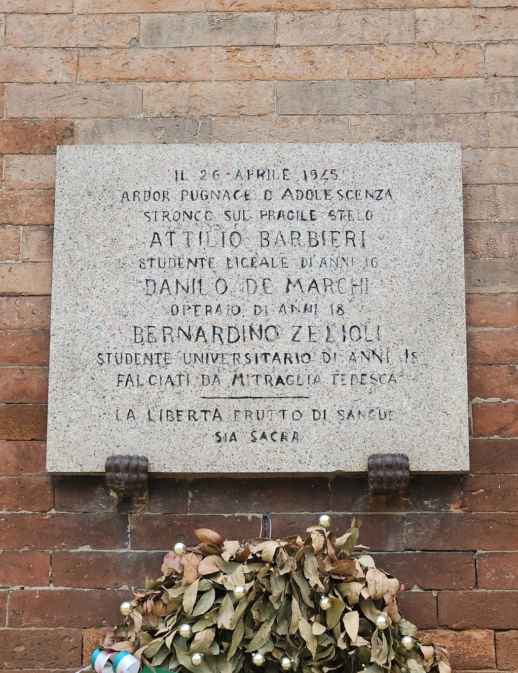 Lapide commemorativa in onore di Attilio Barbieri, Danilo De Marchi e Bernardino Zelioli, con fiori allogati.