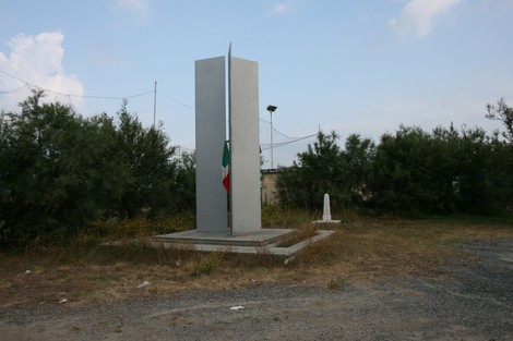 Vecchio cippo a Chiesa, monumento circondato da vegetazione e con bandiera italiana.