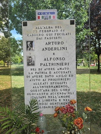 Monumento commemorativo ad Anderlini e Paltrinieri, con fiori e un contesto verde e alberato.