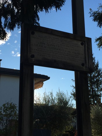 Monumento dedicato a Dini e Salvalai, situato in un contesto naturale illuminato dal sole.