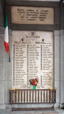 Monumento commemorativo ai caduti partigiani, con nomi incisi e decorazioni floreali in omaggio.
