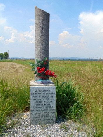 Cippo commemorativo dedicato ai caduti della Resistenza, decorato con fiori rossi, immerso nella natura.