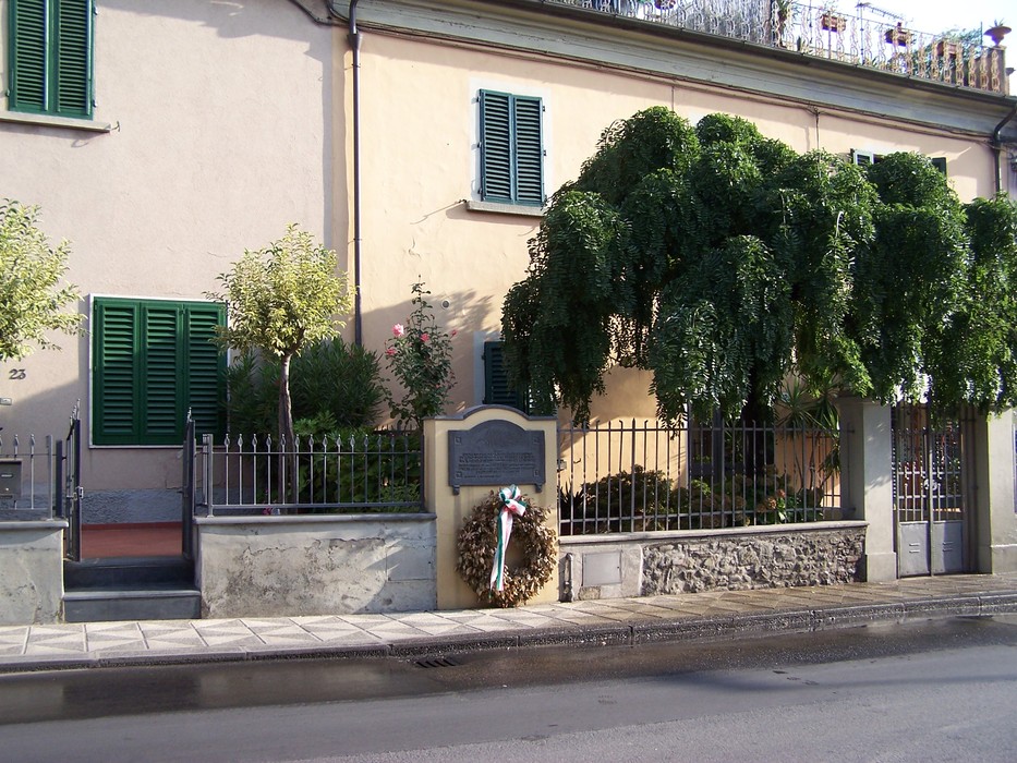 Lapide commemorativa dedicata ai cinque martiri, situata in un contesto urbano con vegetazione.