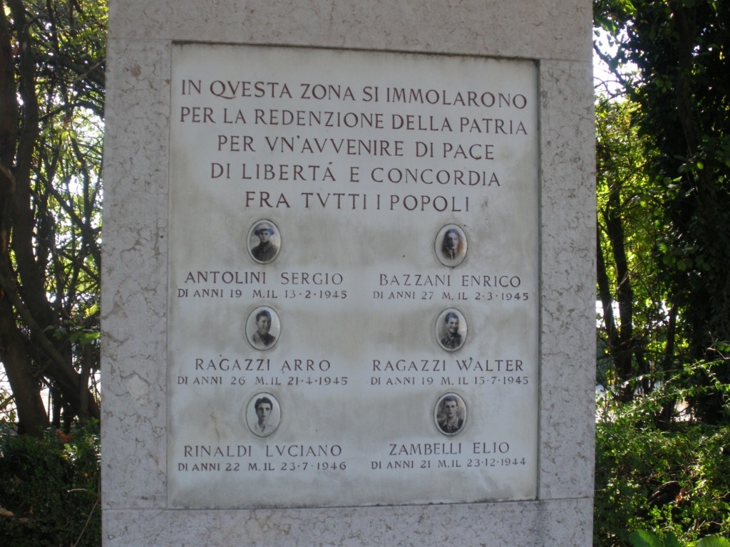 Cippo commemorativo dedicato ai caduti, con nomi e date, circondato da vegetazione in via Castelfranco.