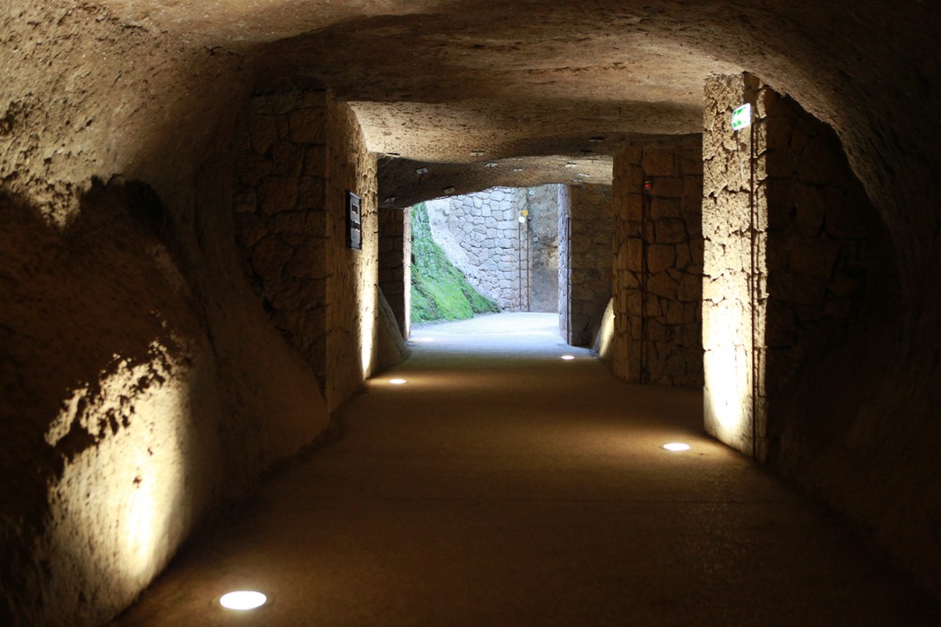 Galleria sotterranea delle Fosse Ardeatine, con pareti in pietra e illuminazione versatile. Atmosfera di memoria e riflessione.