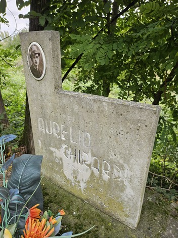 Cippo commemorativo di Aurelio Ghirardi, circondato da vegetazione e decorazioni floreali.