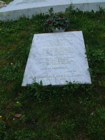Sepolcro del Comandante Memo, commemorazione in marmo con fiori e scritte, immerso nel verde.