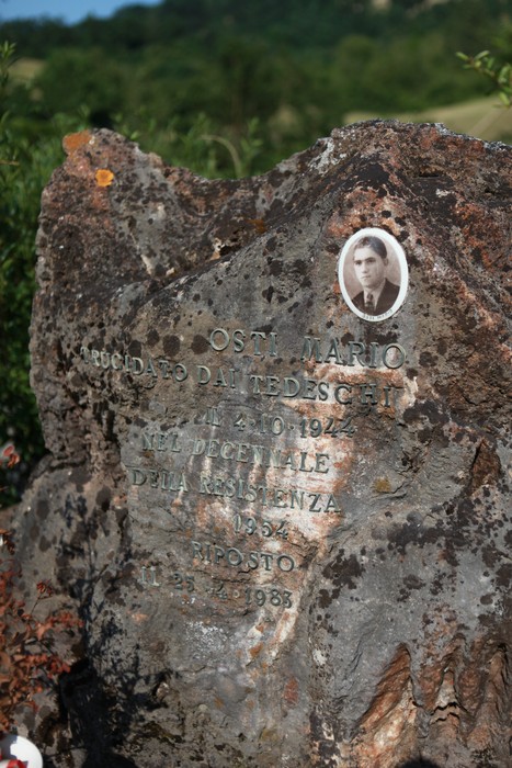 Monumento a Osti, commemorativo con foto e iscrizioni, situato in un contesto naturale.