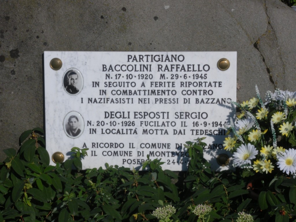 Cippo commemorativo dedicato ai partigiani, con fotografie e date significative, immerso nella natura di Montebudello.