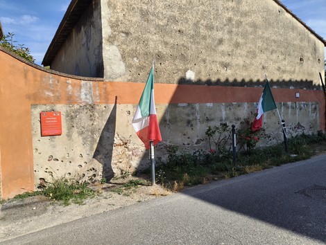 Muro commemorativo dell'eccidio di Pettori, con bandiere italiane e insegne memoriali.