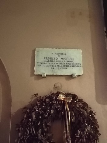 Lapide commemorativa di Ernesto di Micheli, martire della libertà, con corona di fiori.
