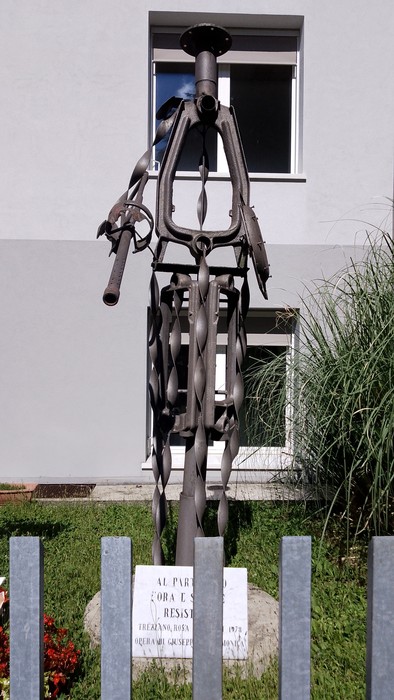 Monumento al partigiano, scultura in metallo che rappresenta un combattente della Resistenza, sullo sfondo di un edificio.