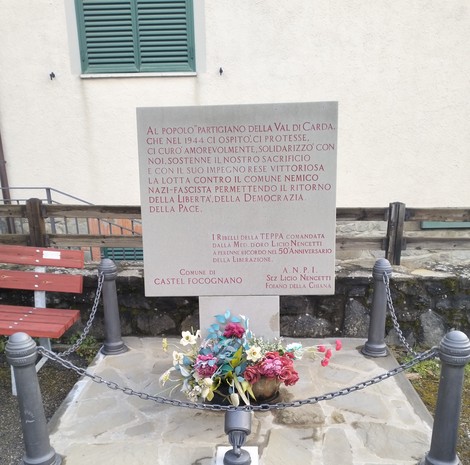 Monumento commemorativo ai partigiani della Val di Carda, con fiori e una targa dedicata alla resistenza.