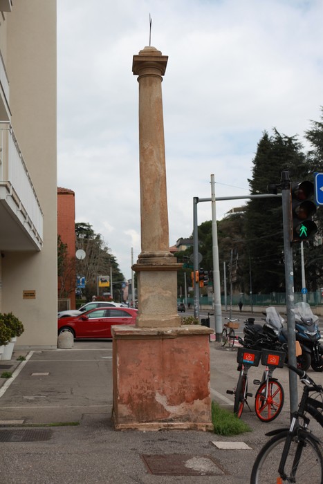 Lapide in pietra monumentale su basamento, situata in un contesto urbano, accanto a una strada.