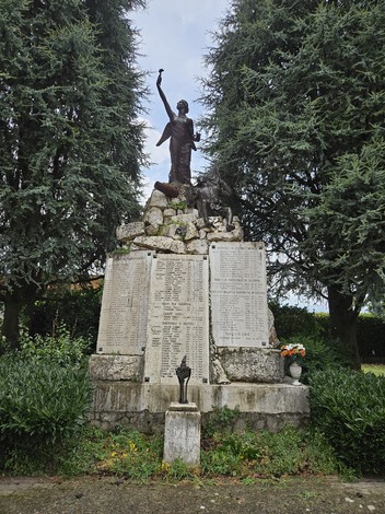 Monumento ai Caduti di Pozzaglio avvolto da verde, con una statua e lapidi commemorative.