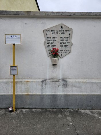 Lapide commemorativa dedicata ai caduti per la libertà, con decorazioni floreali e un messaggio di onore.