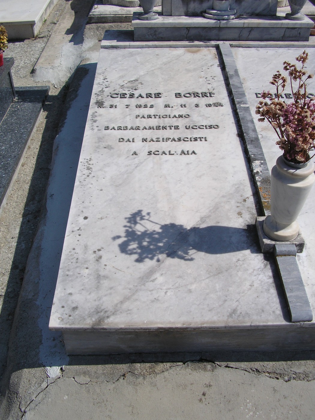 Tomba di Cesare Borri, partigiano ucciso dai nazifascisti, con dettagli in marmo e decorazioni floreali.