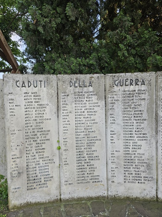 Monumento ai Caduti con nomi incisi in memoria dei soldati, circondato da alberi e vegetazione.