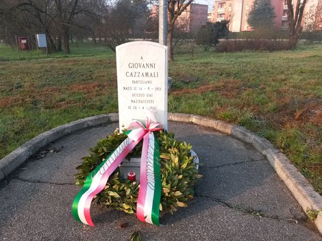 Cippo commemorativo dedicato a Giovanni Cazzamali, partigiano ucciso dai nazifascisti. Di fronte a un paesaggio verde.