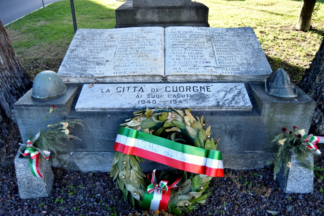 Monumento ai caduti con iscrizioni commemorative e un alloro, immerso nel verde.