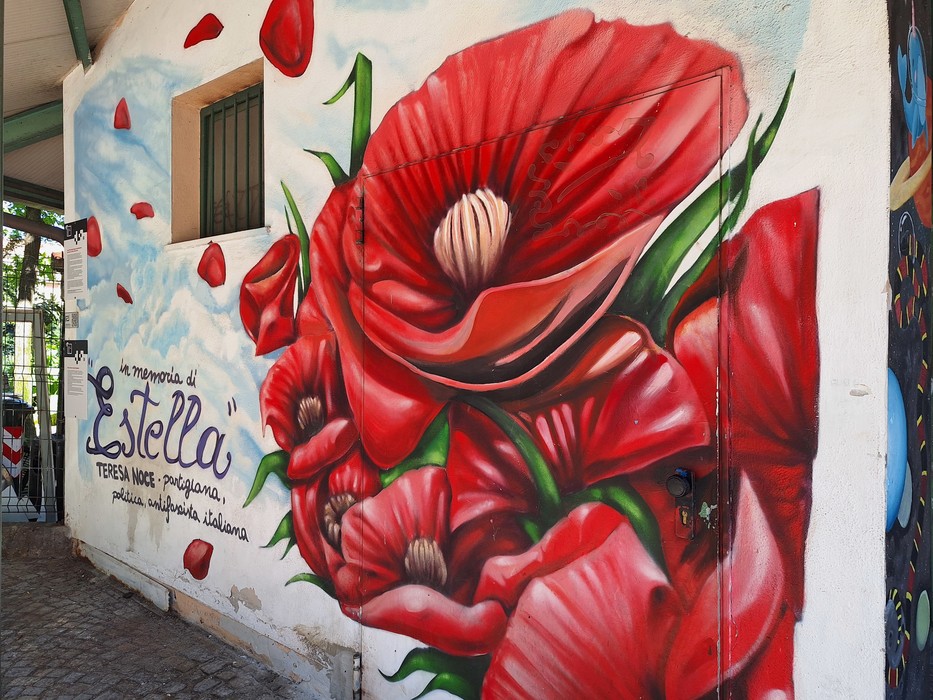 Murale colorato con grandi fiori rossi su una parete, in un'atmosfera vivace e artistica.