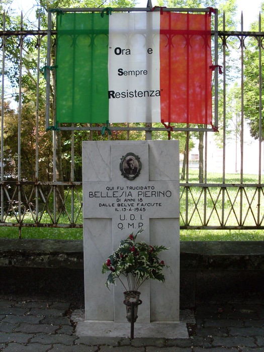 Cippo commemorativo a Bellesia, in onore della Resistenza, con decorazioni e fiori.
