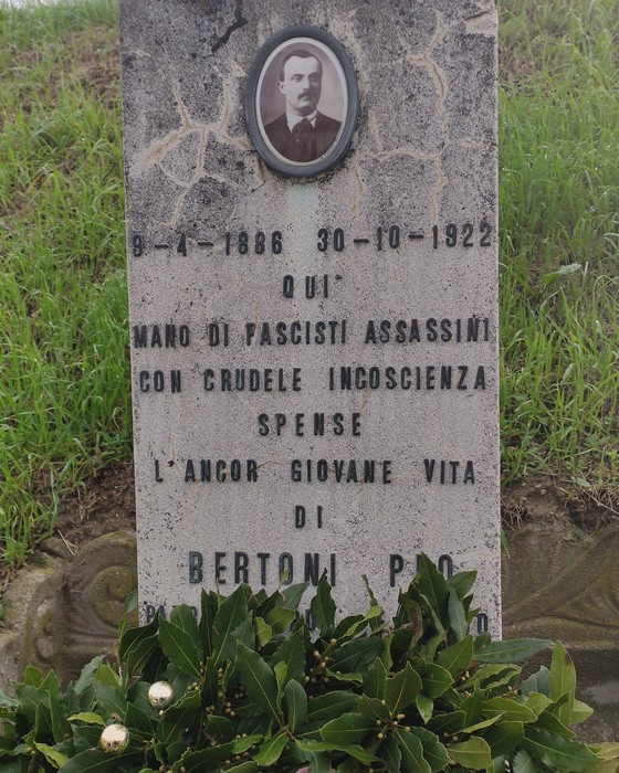 Cippo commemorativo dedicato a Bertoni, vittima di fascismo, con datario e omaggio floreale.