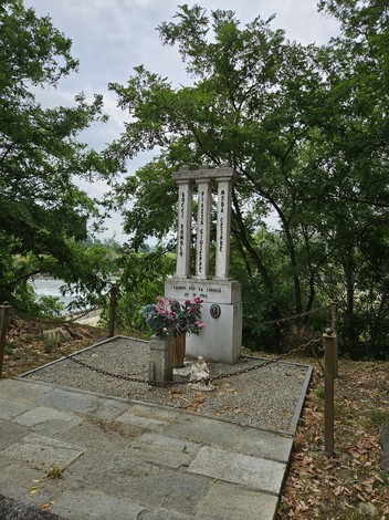 Cippo commemorativo con colonne bianche, fiori e decorazioni, immerso nella vegetazione a Bocci, Piazza e Meda.